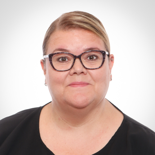 Suvi katsoo suoraan kameraan. Vaaleat hiukset ja mustareunaiset silmälasit.